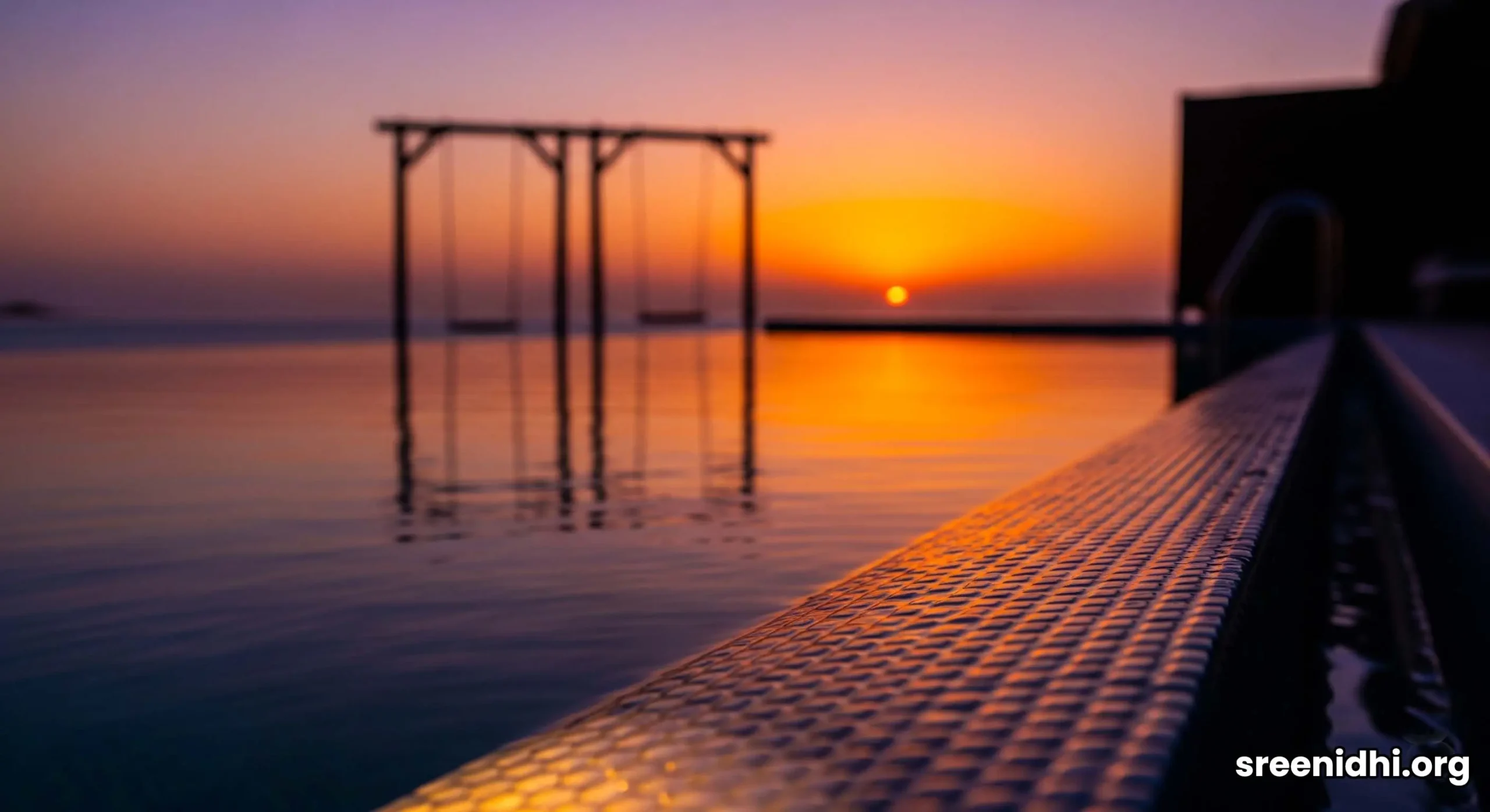 A private water villa on Nurai Island at sunset, featuring a glowing infinity pool and iconic over-water swings.